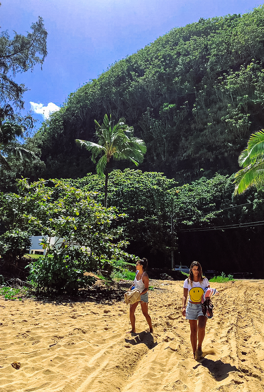 alt="Two Girls Walking On a Sandy Beach Surrounded by Lush Greenery in Kauai, Hawaii"