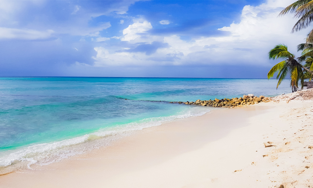 alt="blue sea with rocks dipping into water and white sand along the shore"