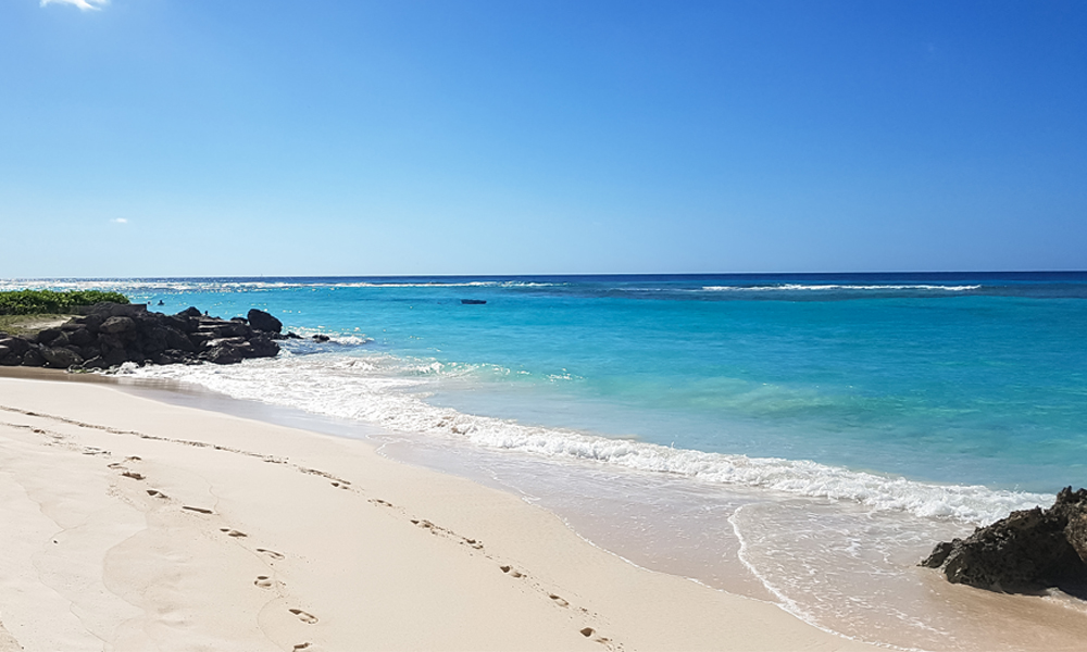 alt="White sand beach with blue sea water surrounded by rocks in Barbados"