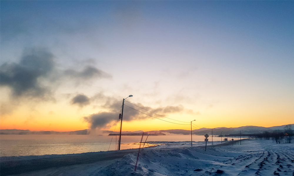 alt=“Low clouds that look like smoke and sunset over the sea in Gibostad town, Northern Norway”