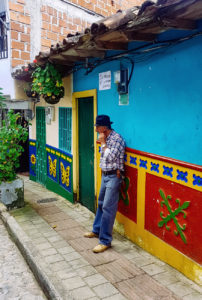 alt="Man standing outside colourful painted house in Guatape, Colombia"