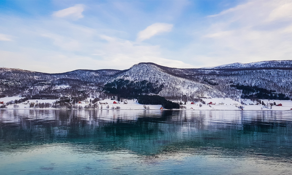 alt=“Snowy mountain landscape and blue lake Gibostad town, Northern Norway”