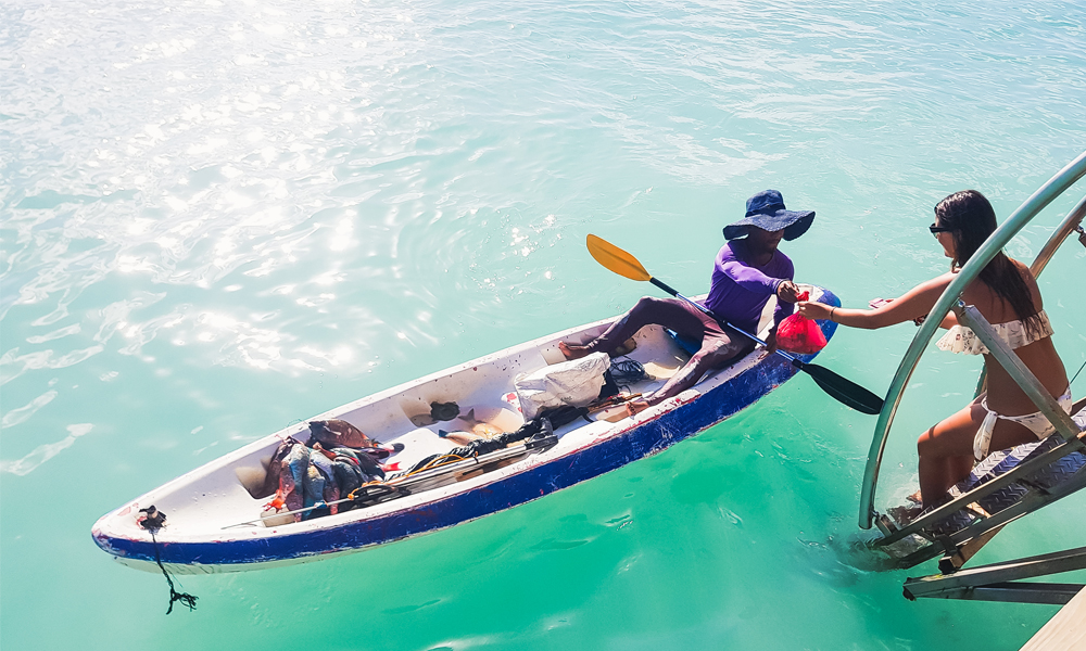 alt="Paper Pelicans girl buying fish from fisherman at Bayahibe beach"