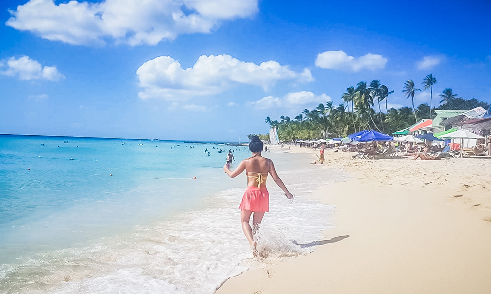 alt="Paper Pelicans girl walking along shore on the beach at Bayahibe"