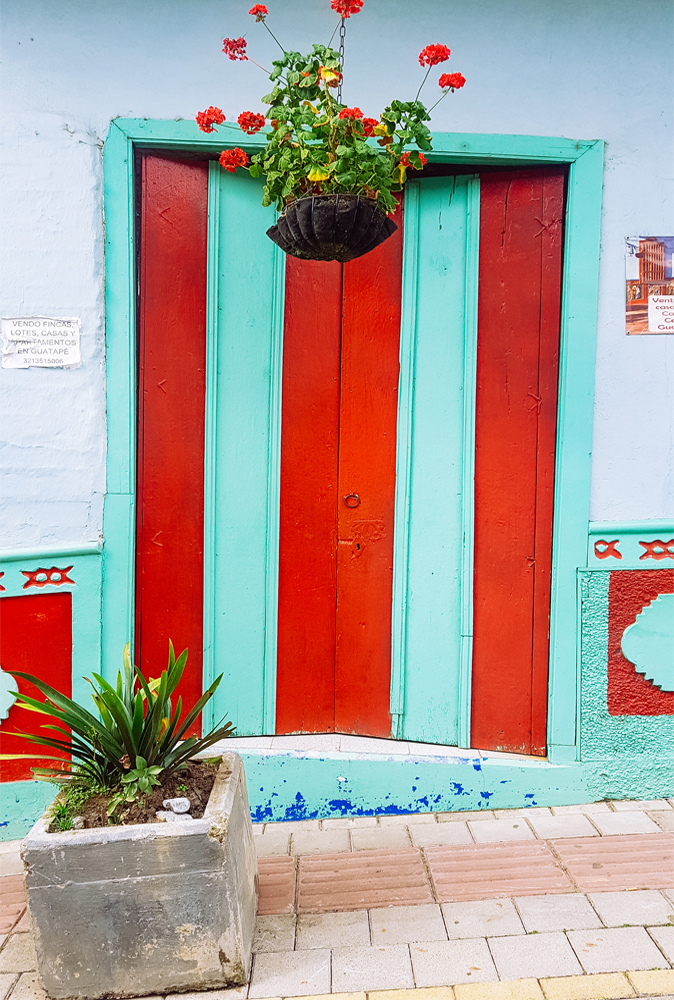 alt="Red and turquoise door with red flowers hanging on top in Guatape, Colombia"
