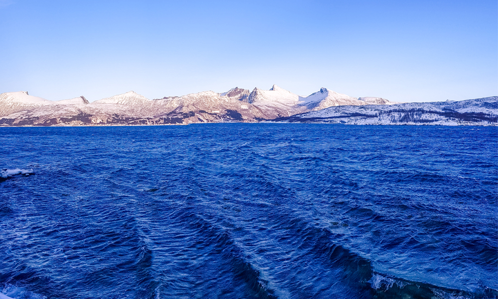 alt=“Waves and snowy mountains peaks in Northern Norway”