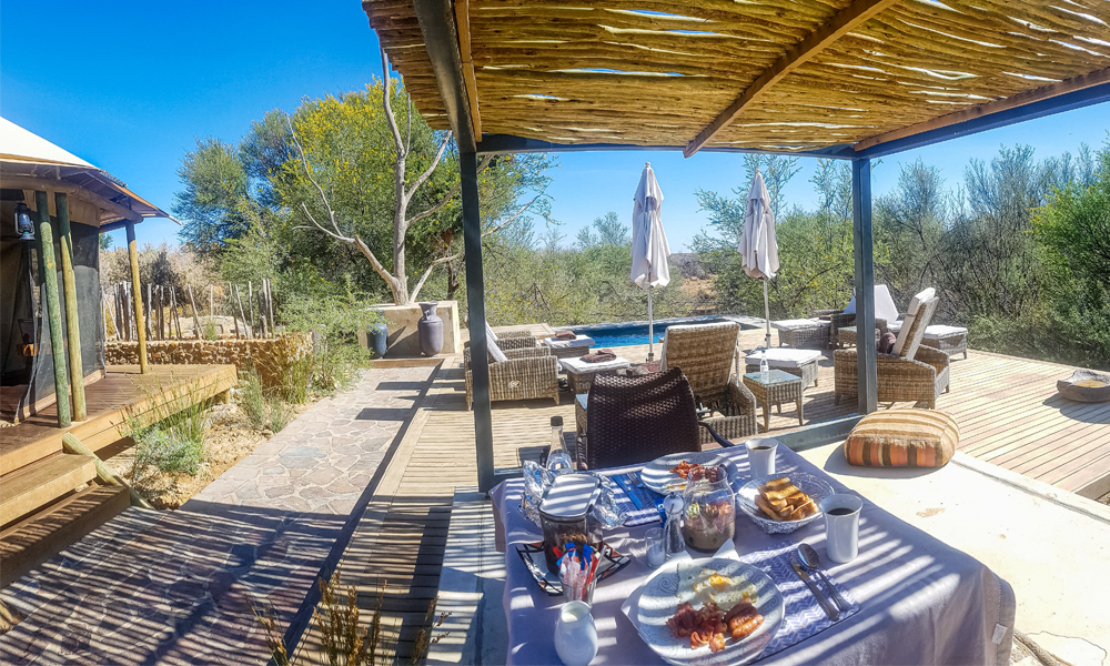 alt="Kuganha tented safari outdoor breakfast with eggs, sausages and orange juice at Inverdoorn Game Reserve"