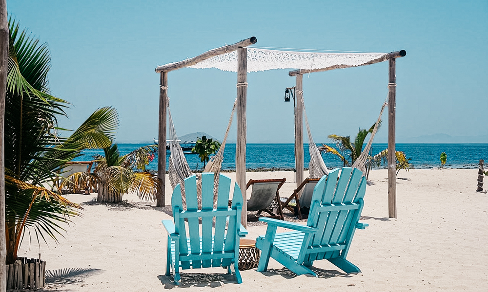 alt=“le-pirate-hammocks-on-beach-with-blue-chairs”