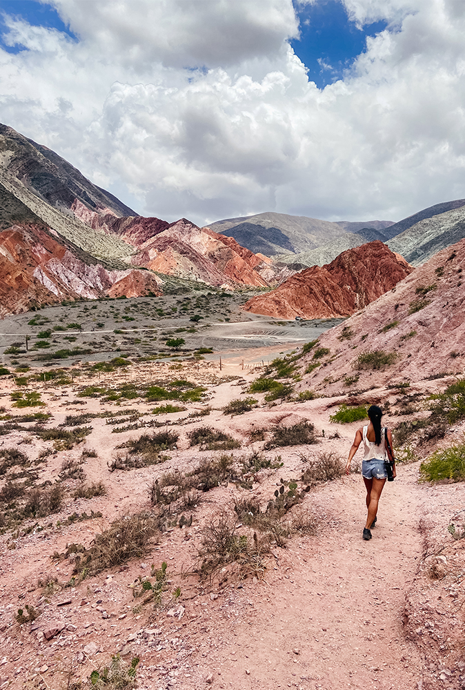 alt="Girl Carrying Camera And Walking Across the Paseo de Los Colorados Multi Coloured Mountains"