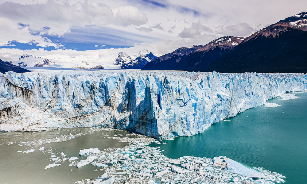 alt=“Perito Moreno glacier front view with split rivers and ice broken into the water”