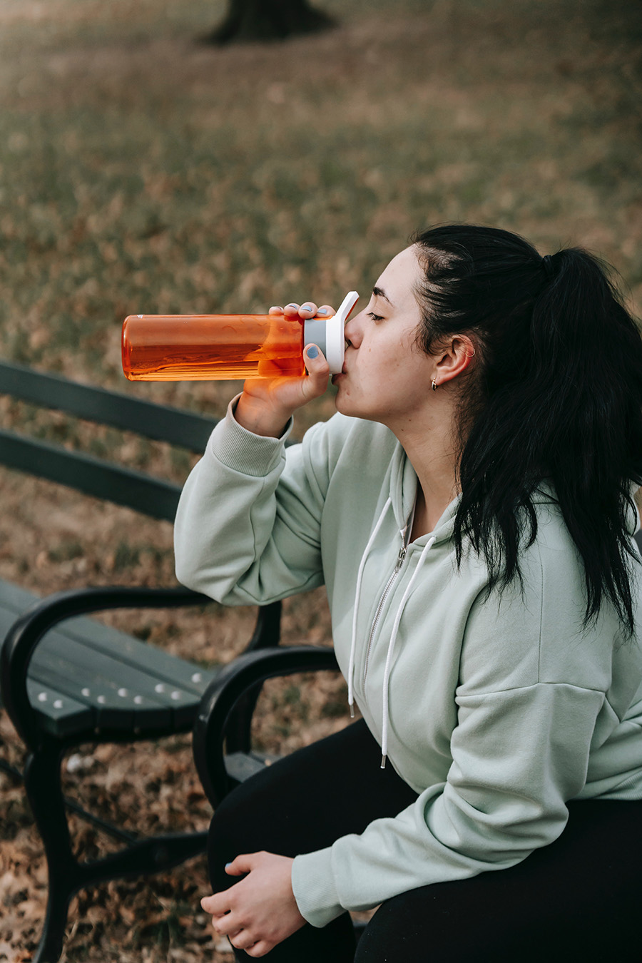 woman-sitting-on-bench-drinking-water